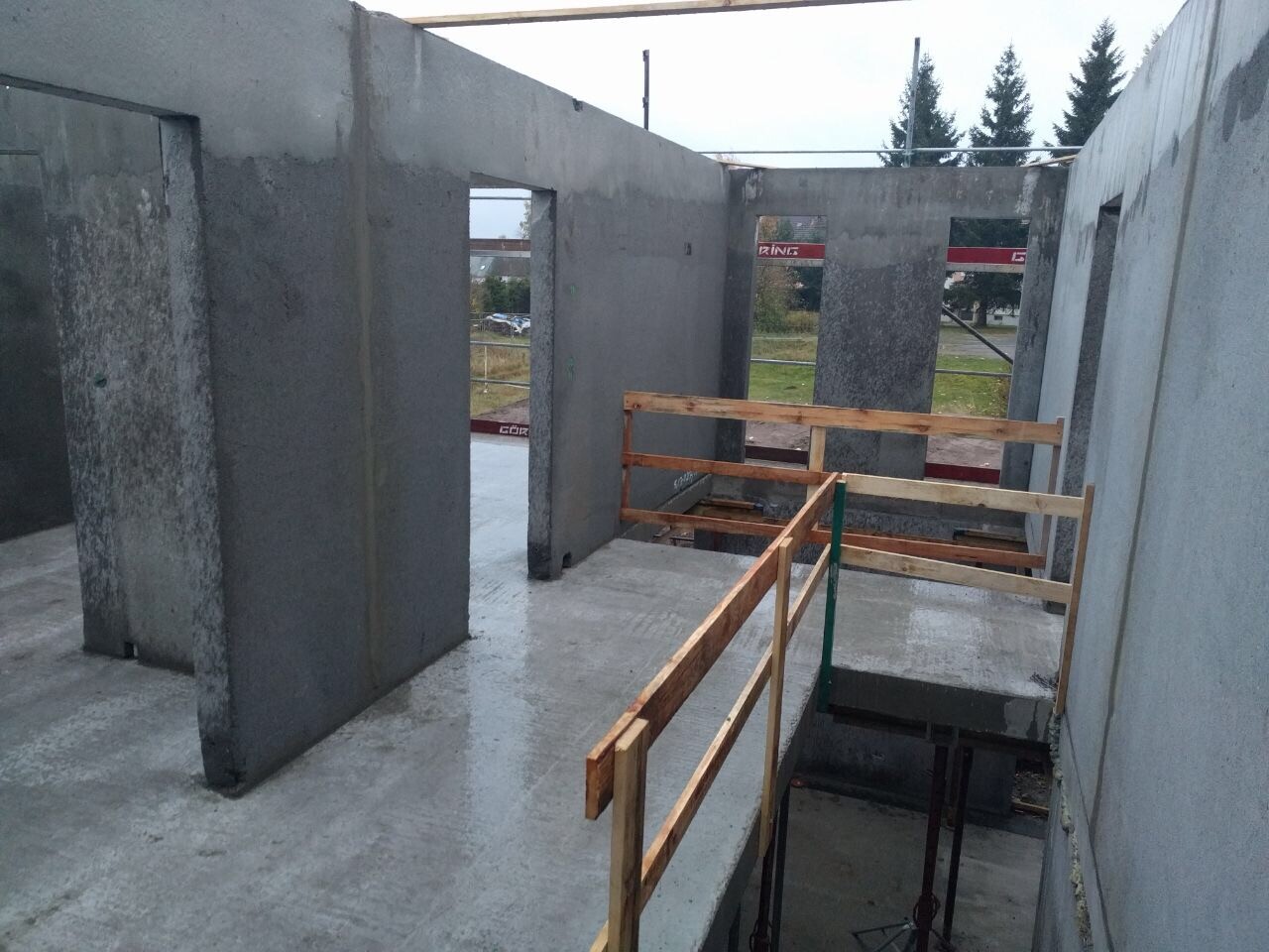 Rohbau eines Betongebäudes mit offenen Wänden und Holzgeländern um eine Absturzöffnung.