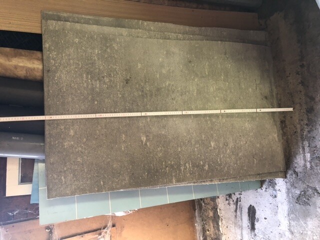 Große graue Platte mit Messband darauf, liegt auf weiteren Platten in einer Werkstatt.