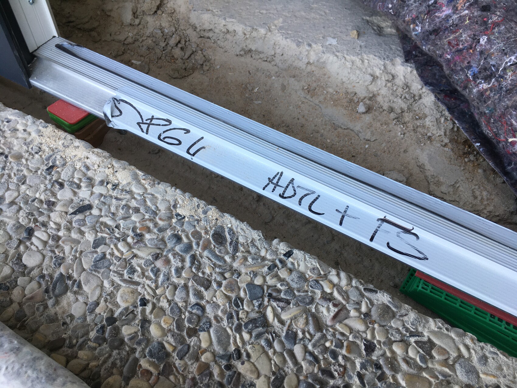 Lange silberne Metall-Schiene liegt quer auf Kies neben einer Bauöffnung, mit Marker beschriftet