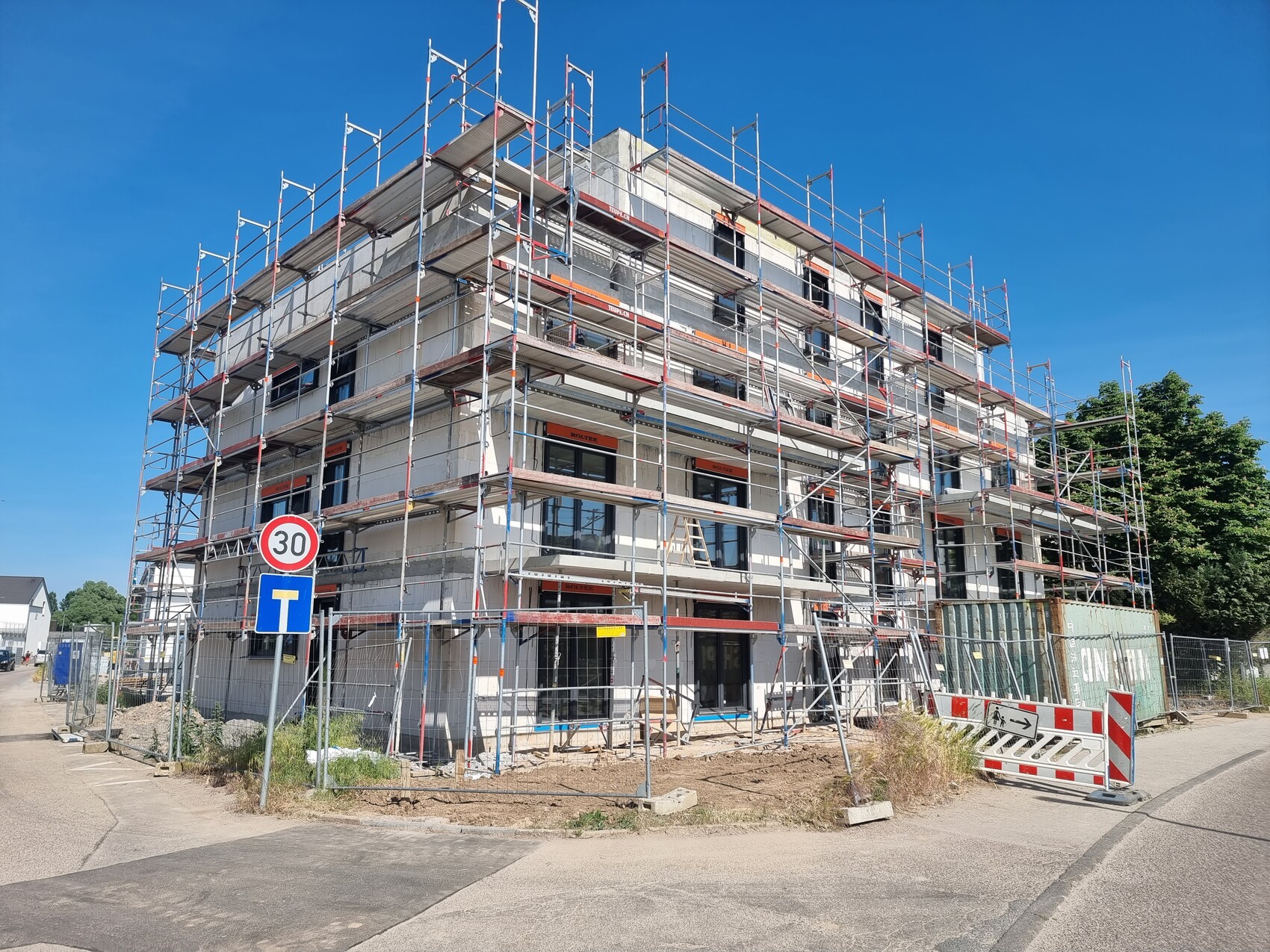 Neubau mit mehrstöckigem Gerüst umgeben von Absperrungen; Straßenschilder im Vordergrund.