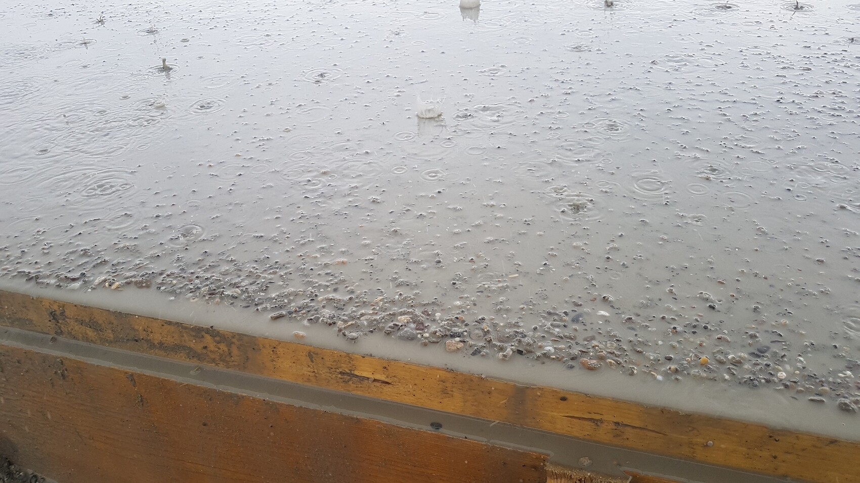 Frisch gegossene Betonoberfläche mit Kieseln und Regen im Rohbau