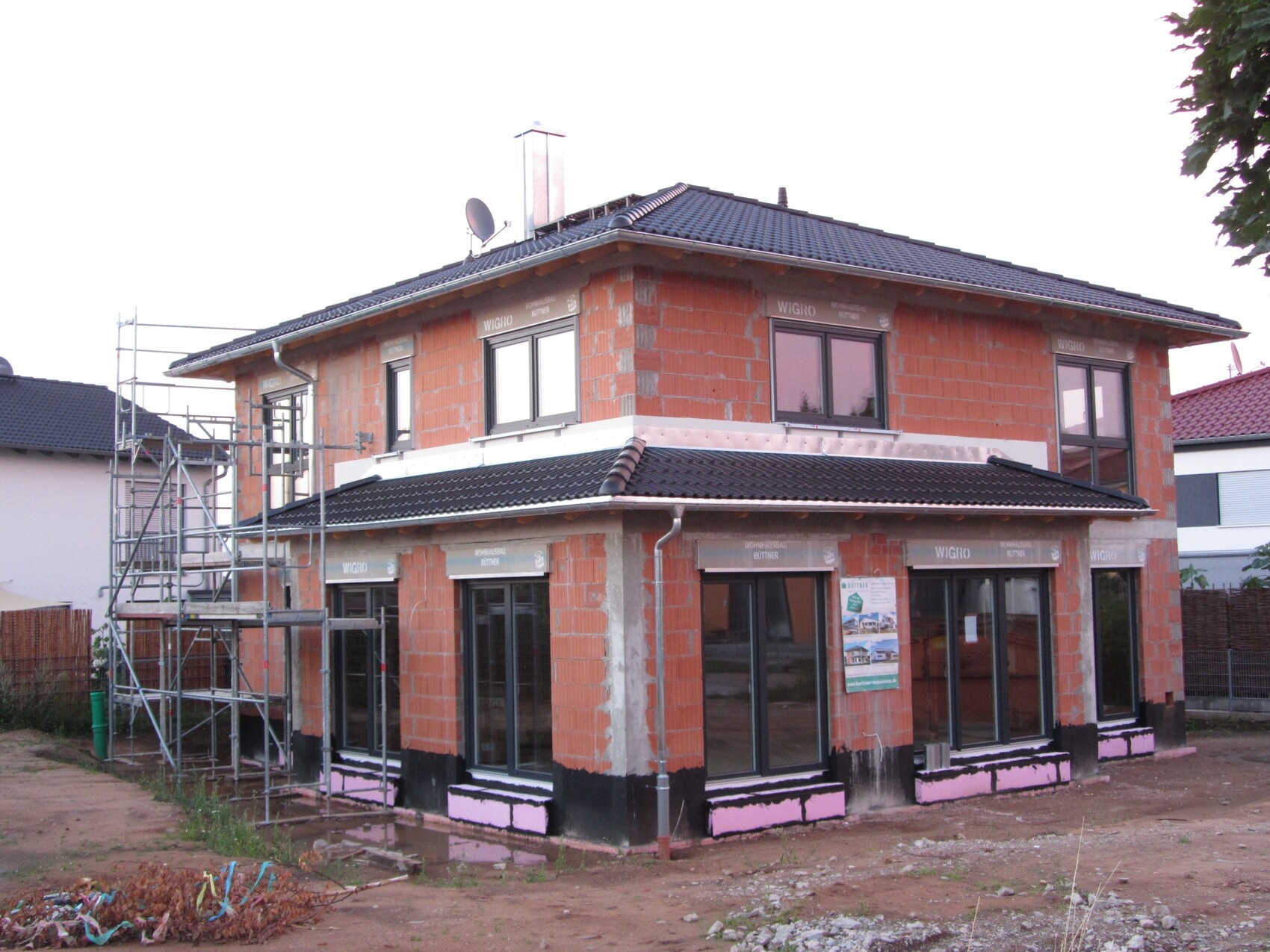 Zweigeschossiges Rohbauhaus aus roten Ziegeln mit Gerüst links und dunklem Dach.