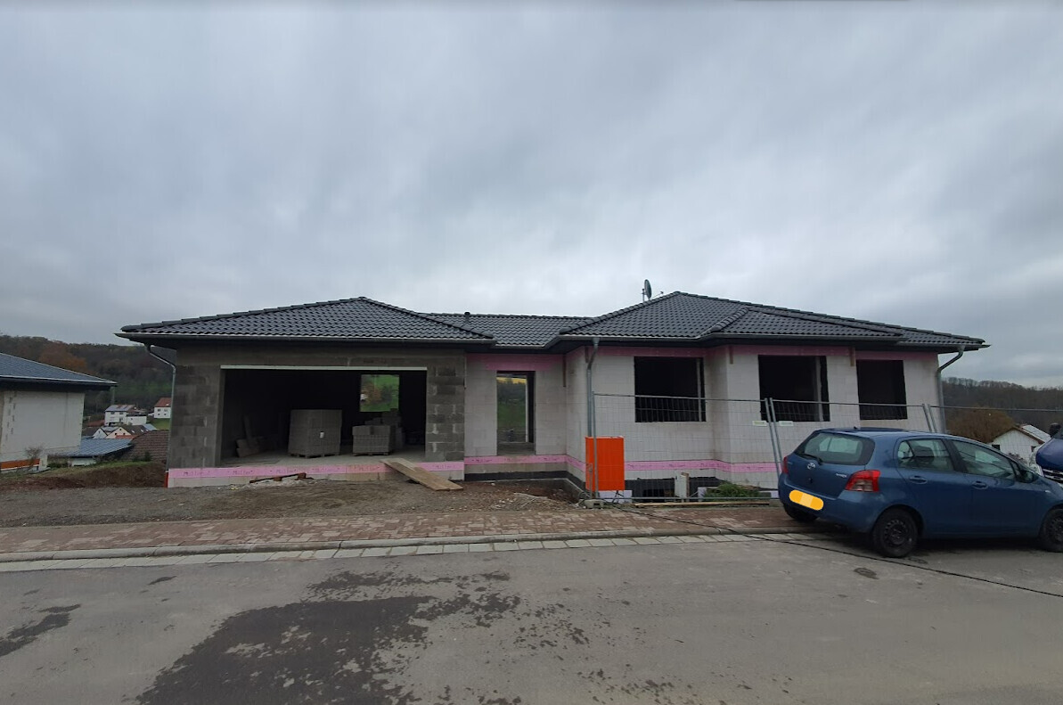 Halbfertiges Einfamilienhaus mit offener Garage, Baumaterialien, pinke Isolierung, blaues Auto davor