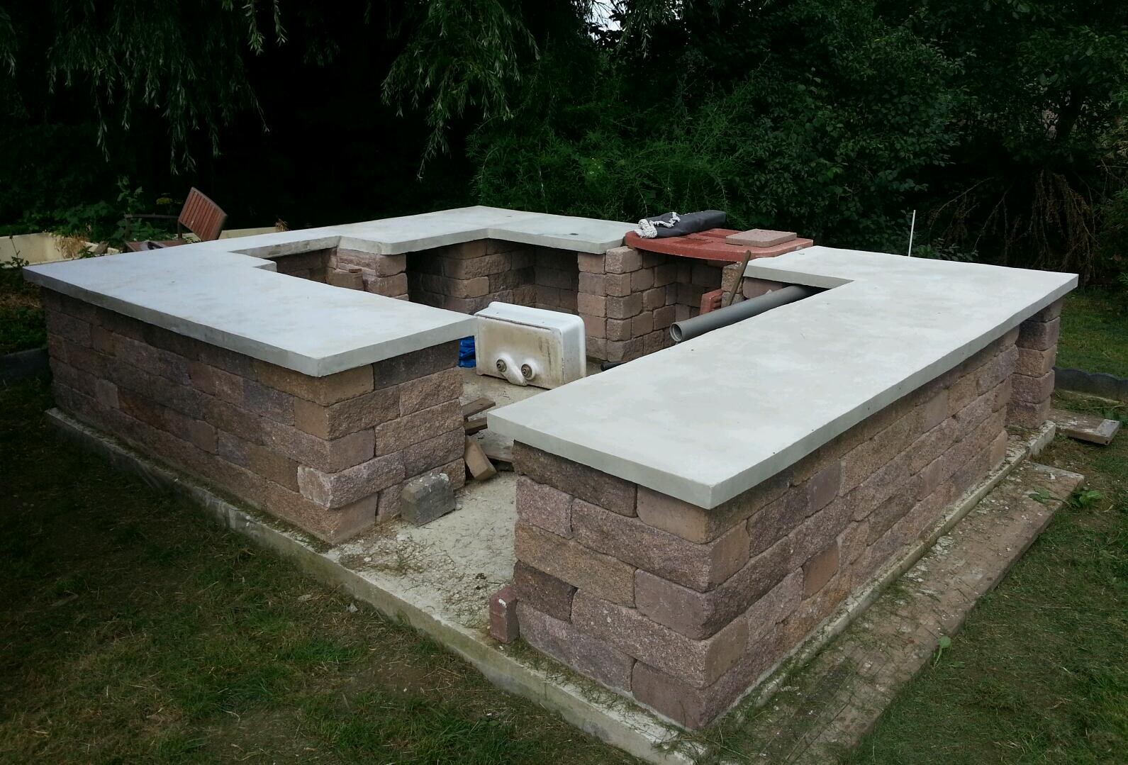 Außenkücheninsel aus Steinfundament mit Betonplatten im Gartenunterbau