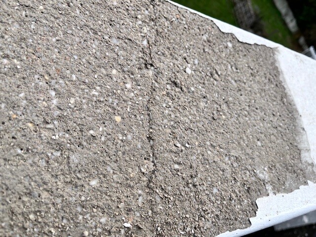 Nahaufnahme einer groben grauen Betonoberfläche mit Körnung und einem weißen Rand.