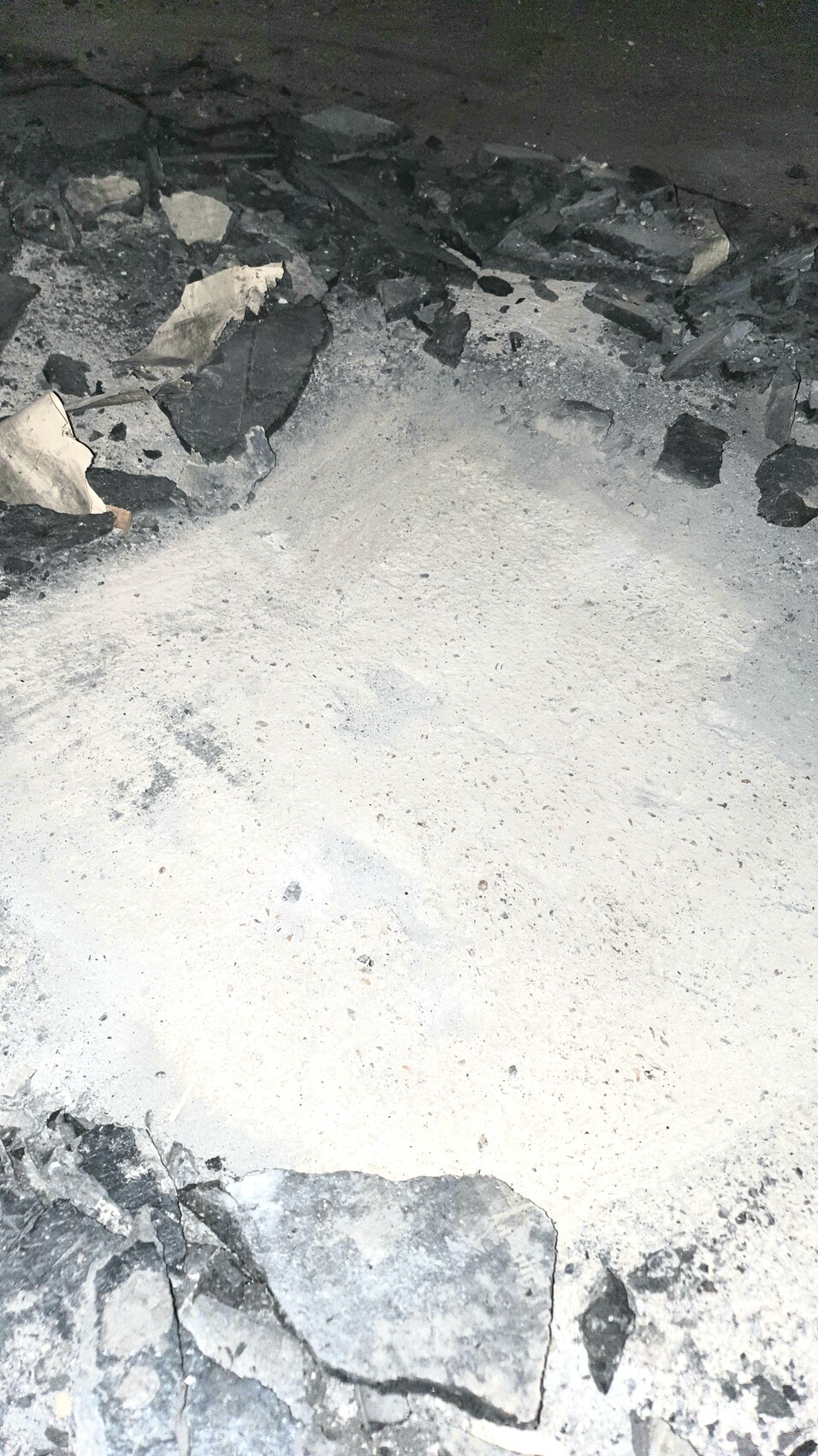 Zerbrochenes Gestein und Staub um eine helle Bodenfläche in einer Grube.