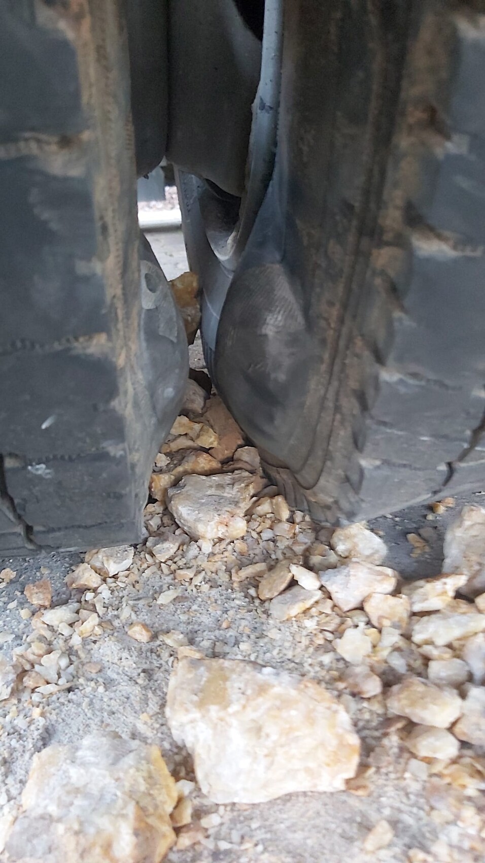 Zwischen zwei groben Offroad-Reifen liegen Kieselsteine auf unbefestigtem Boden.