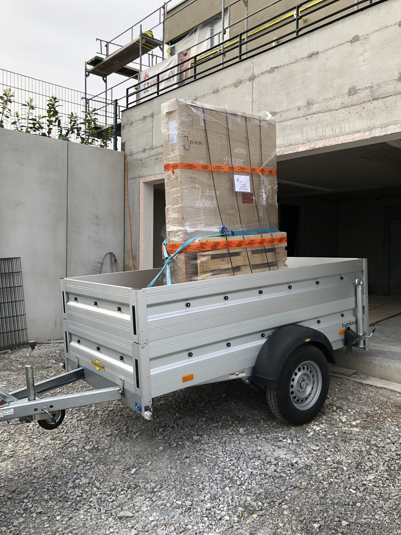 Ein Baustellen-Trailer mit beladenen Palettenboxen, durch orangene Bänder gesichert.
