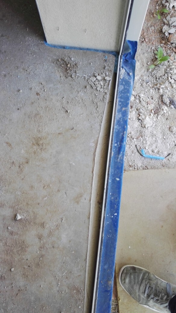 Baustelle mit Türrahmen, blauem Schutzrand, unfertiger Boden und Schuh im Vordergrund