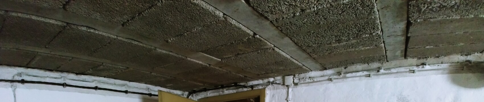 Unbearbeitete Kellergeschoss-Decke aus Sichtbeton mit sichtbaren Rohren an der Wand.