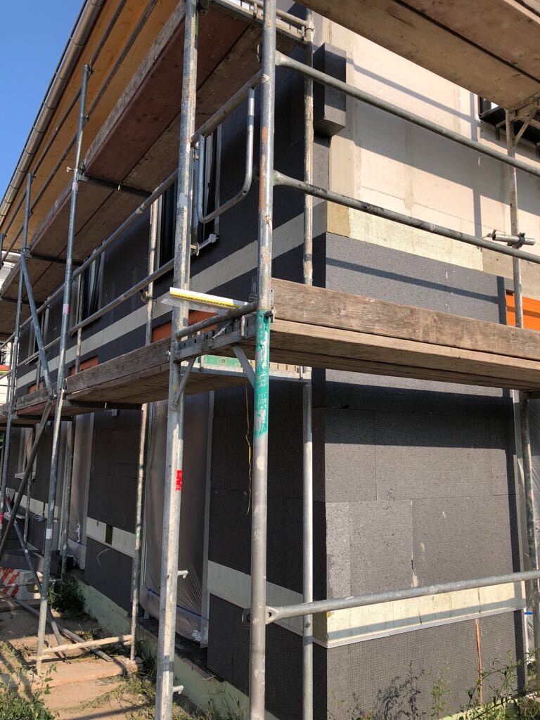 Außenansicht eines Bauprojekts: Gerüst um ein Gebäude mit Dämmplatten an der Fassade.