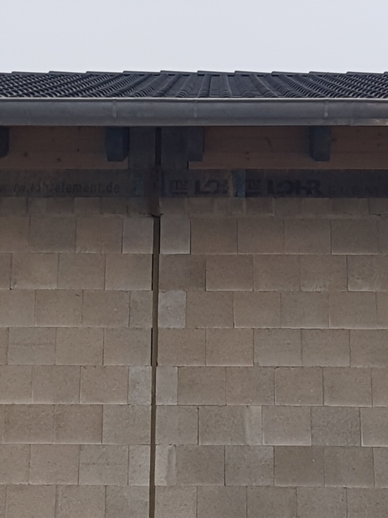 Außenwand aus Betonblöcken mit senkrechtem Riss in der Mitte, Dachüberstand mit Ziegeln.