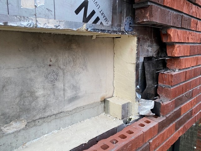 Ziegelwand im Bau, sichtbare Dämmung, Betonunterlage und Baufolie