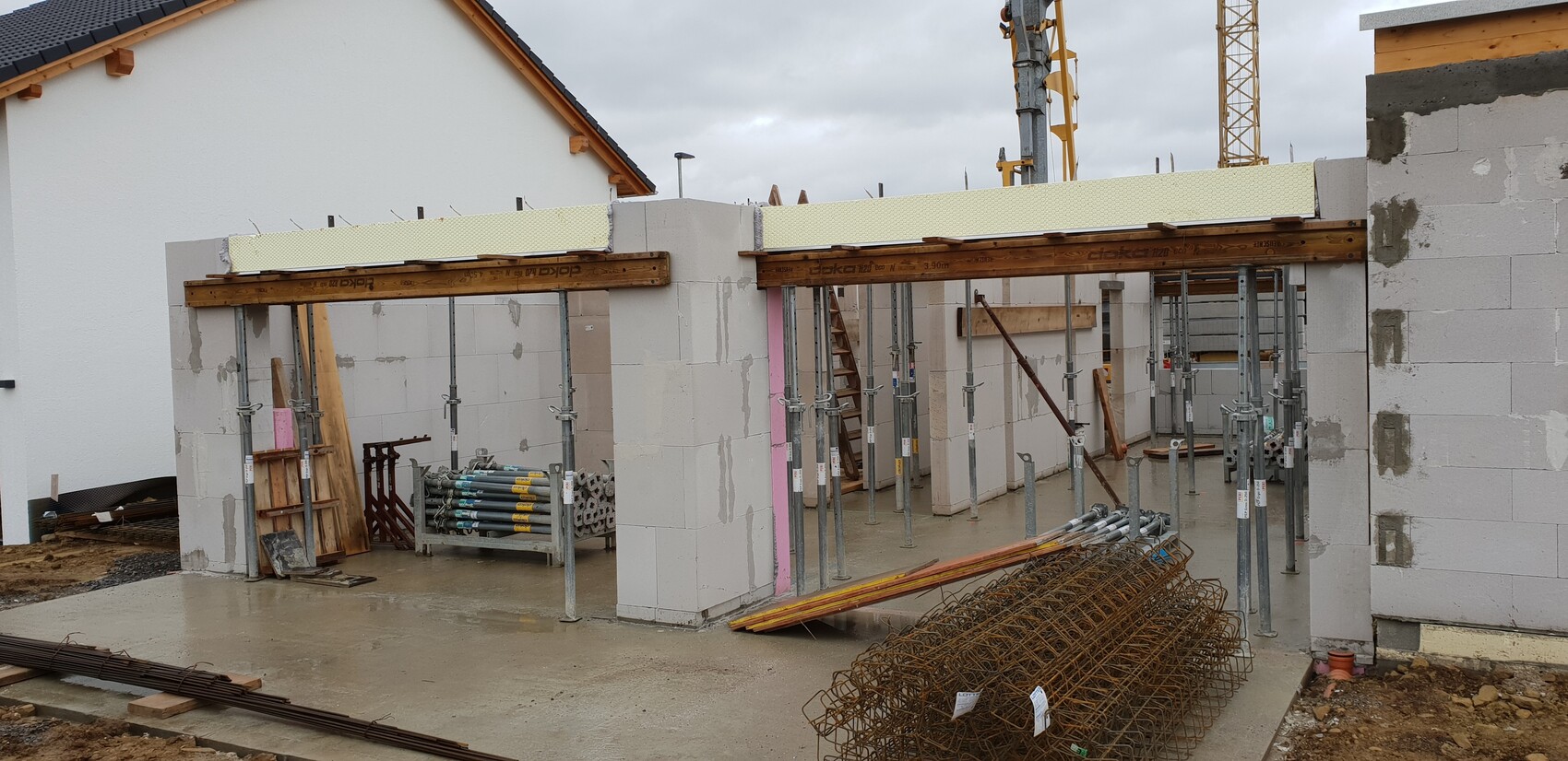 Baustelle mit Betonwänden, Holzträgern, Gerüststützen und Stahlbewehrung; Kran im Hintergrund.