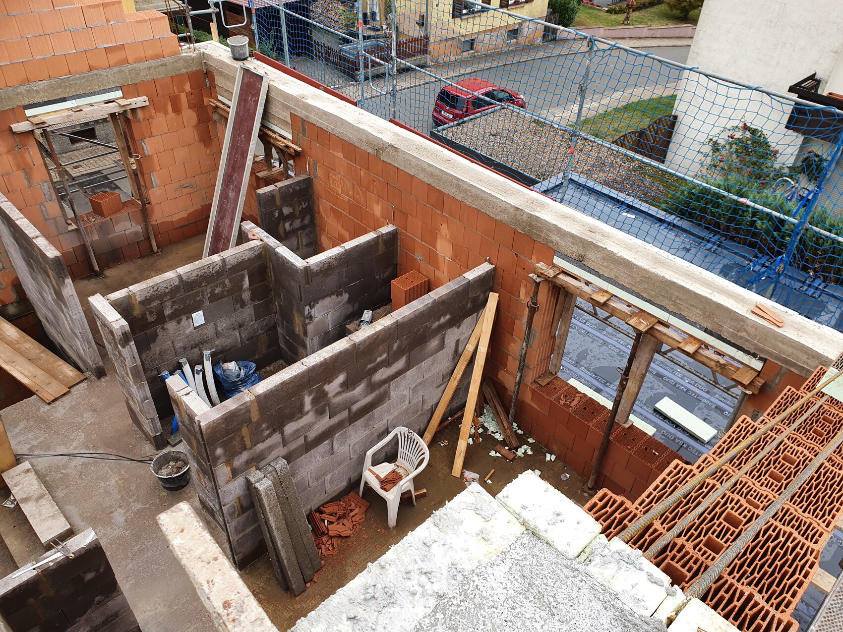 Baustelle mit Ziegel- und Betonwänden, Holzbalken, Plastiksessel und Sicherheitsnetz.
