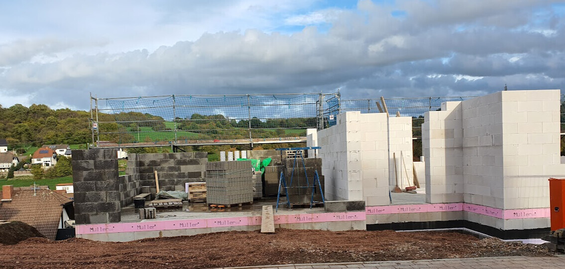 Baustelle mit weißen Porenbetonblöcken, halbfertigen Wänden, Netzschutz und Baumaterialien.