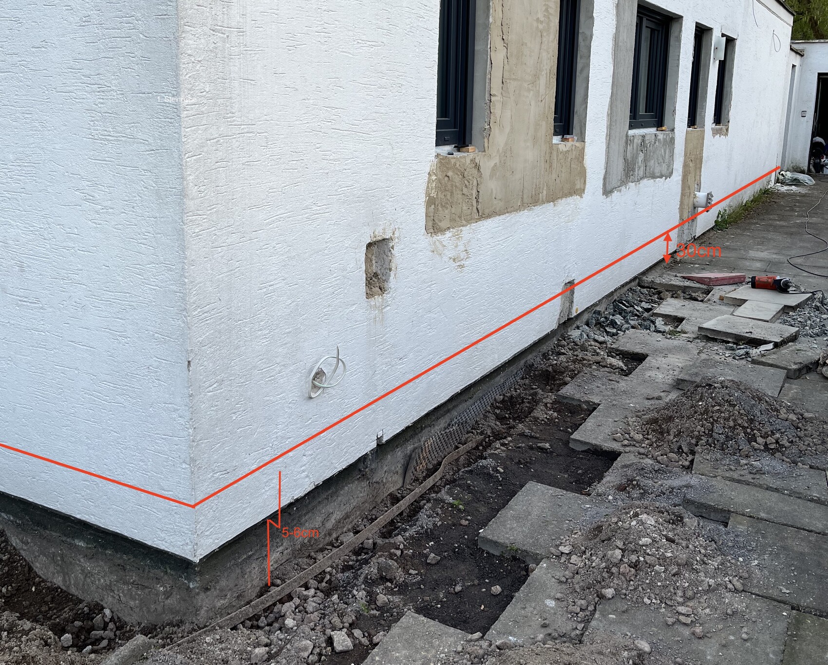 Außenwand eines Hauses mit sichtbar ausgehobenem Fundament und Baugeräten.