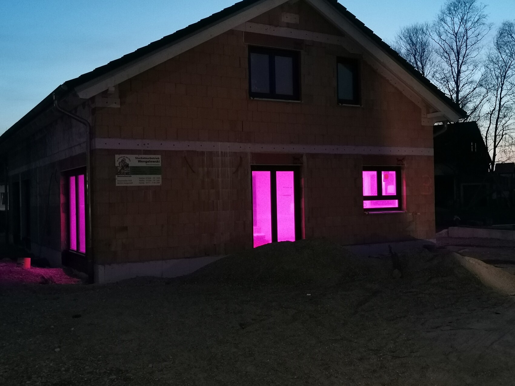 Haus im Bau bei Dämmerung; pink beleuchtete Fenster und Tür.