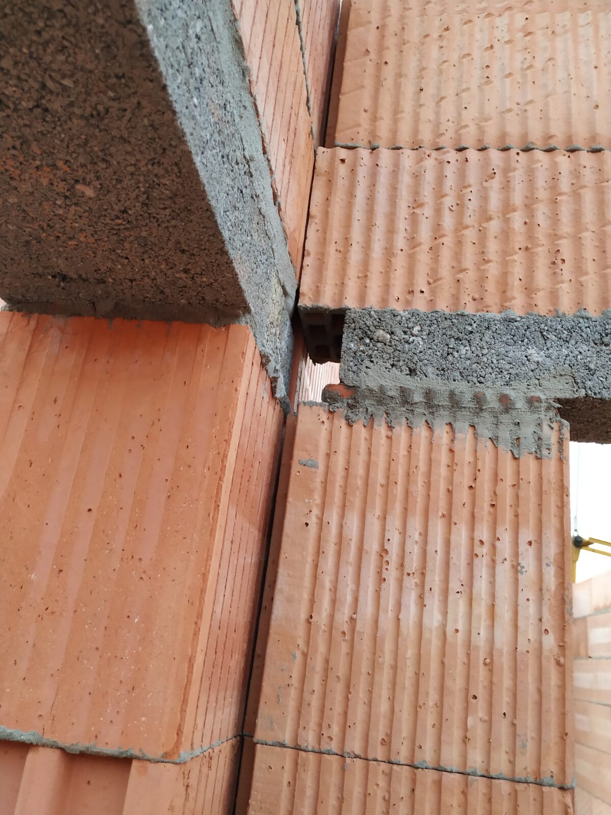Unvollständige Mauer aus orangefarbenen Ziegeln mit grauem Mörtel; Eckverbindung sichtbar.