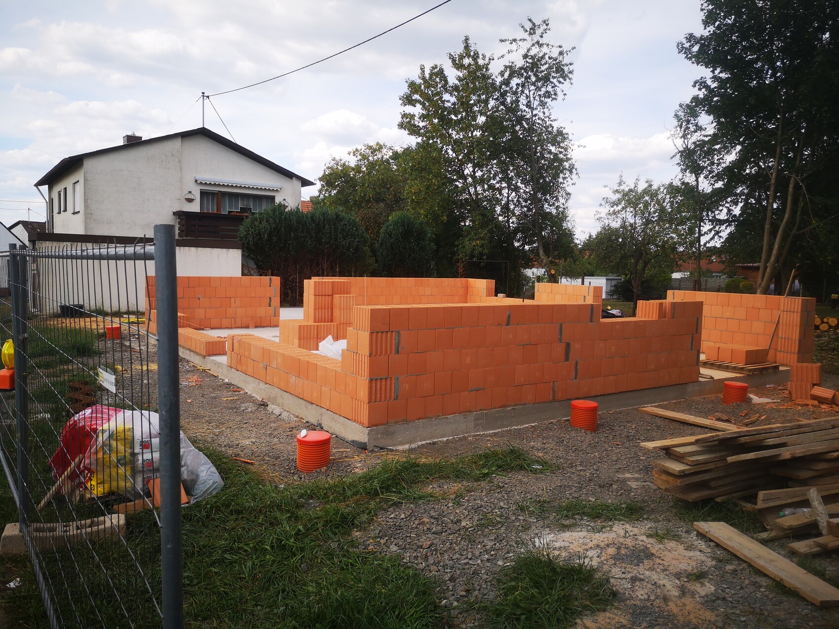 Baustelle mit orangefarbenen Ziegelwänden auf Fundament, Baumaterialien und Haus im Hintergrund.