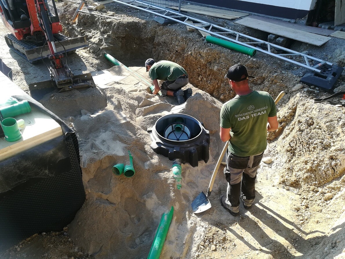 Zwei Bauarbeiter arbeiten in einer Baugrube mit Rohren und Schaufeln