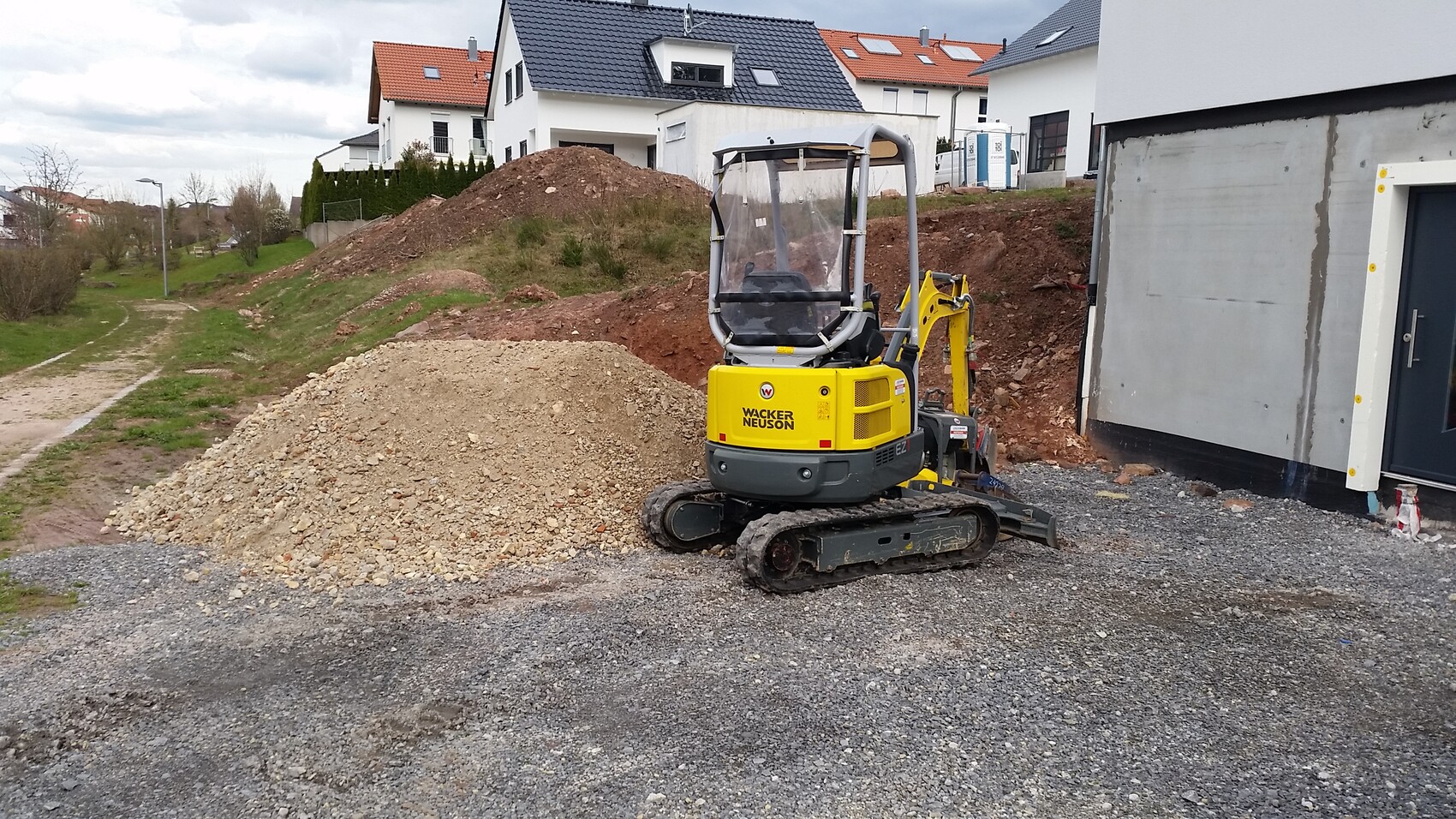 Kleine gelbe Baumaschine (Minibagger) auf einer Baustelle neben einem Neubau mit Erdaushub