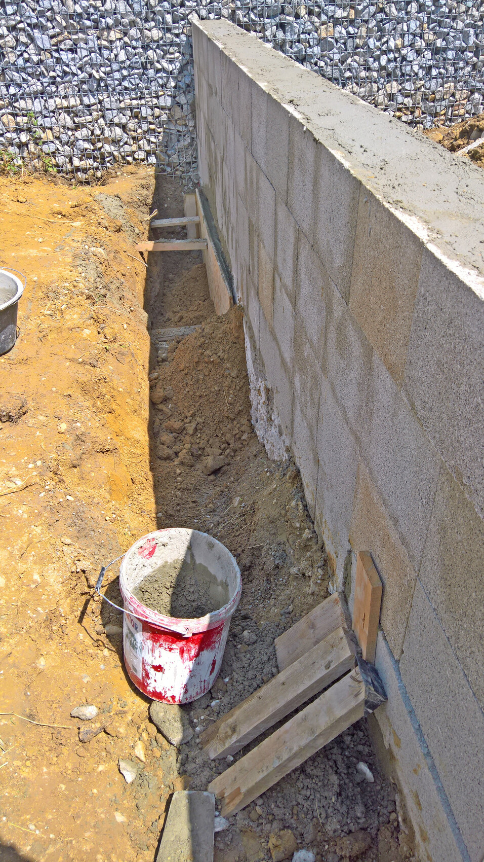 Baugrube neben Betonmauer aus Blöcken; Eimer mit Zement und Holzplanken