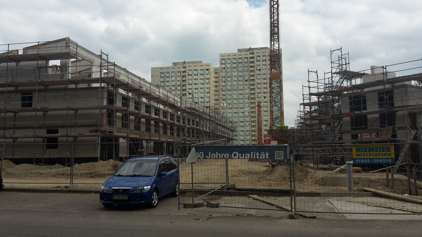Baustelle mit Rohbau, Geruestkonstruktionen, Kran und mehrstockigen Gebaeuden im Hintergrund