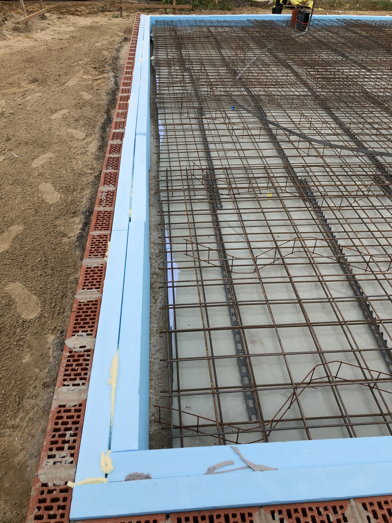 Fundamentplatte mit Bewehrungsstahlgitter, blaue Randformen und Erdarbeiten im Bau.
