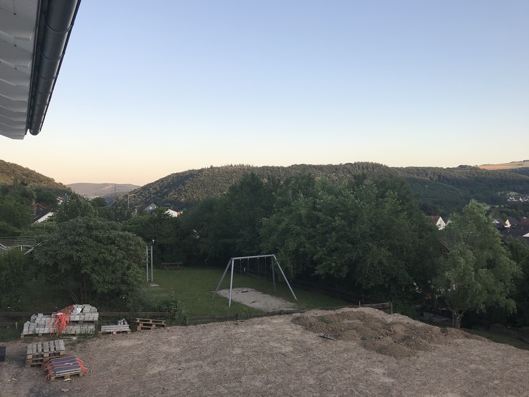 Baustelle im Garten: Erdhügel, Paletten, Spielgeräte, Bäume und Hügel im Hintergrund