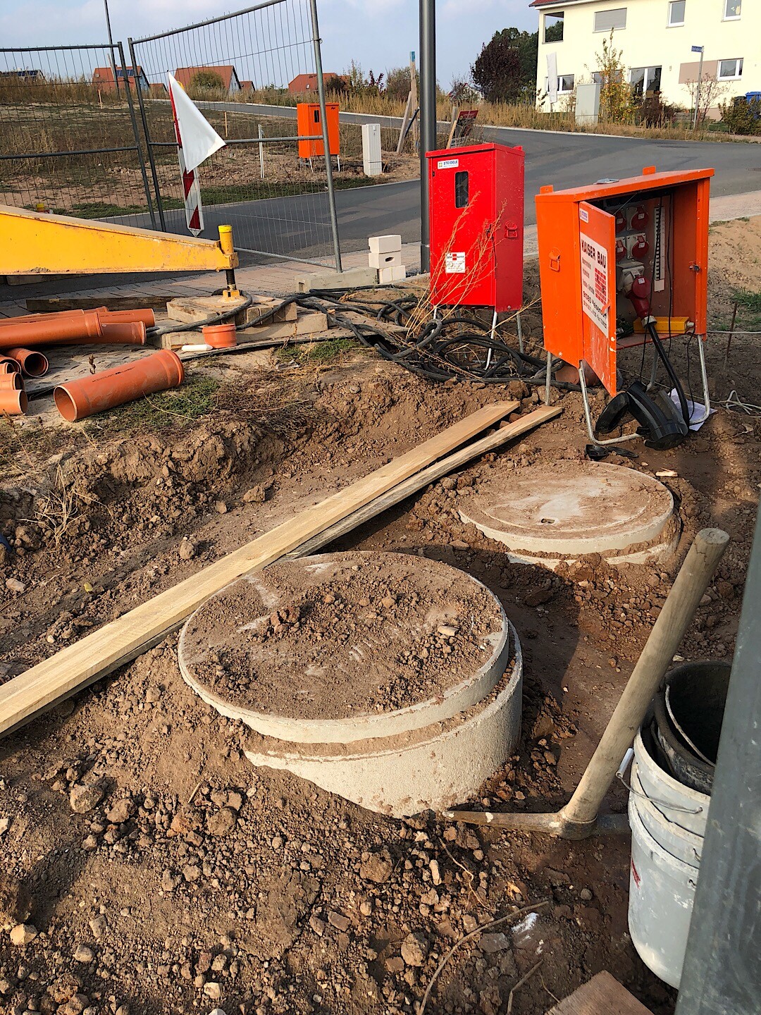 Baustelle mit Rohbaufundamenten, Rohren und orangenen Sicherheitskästen