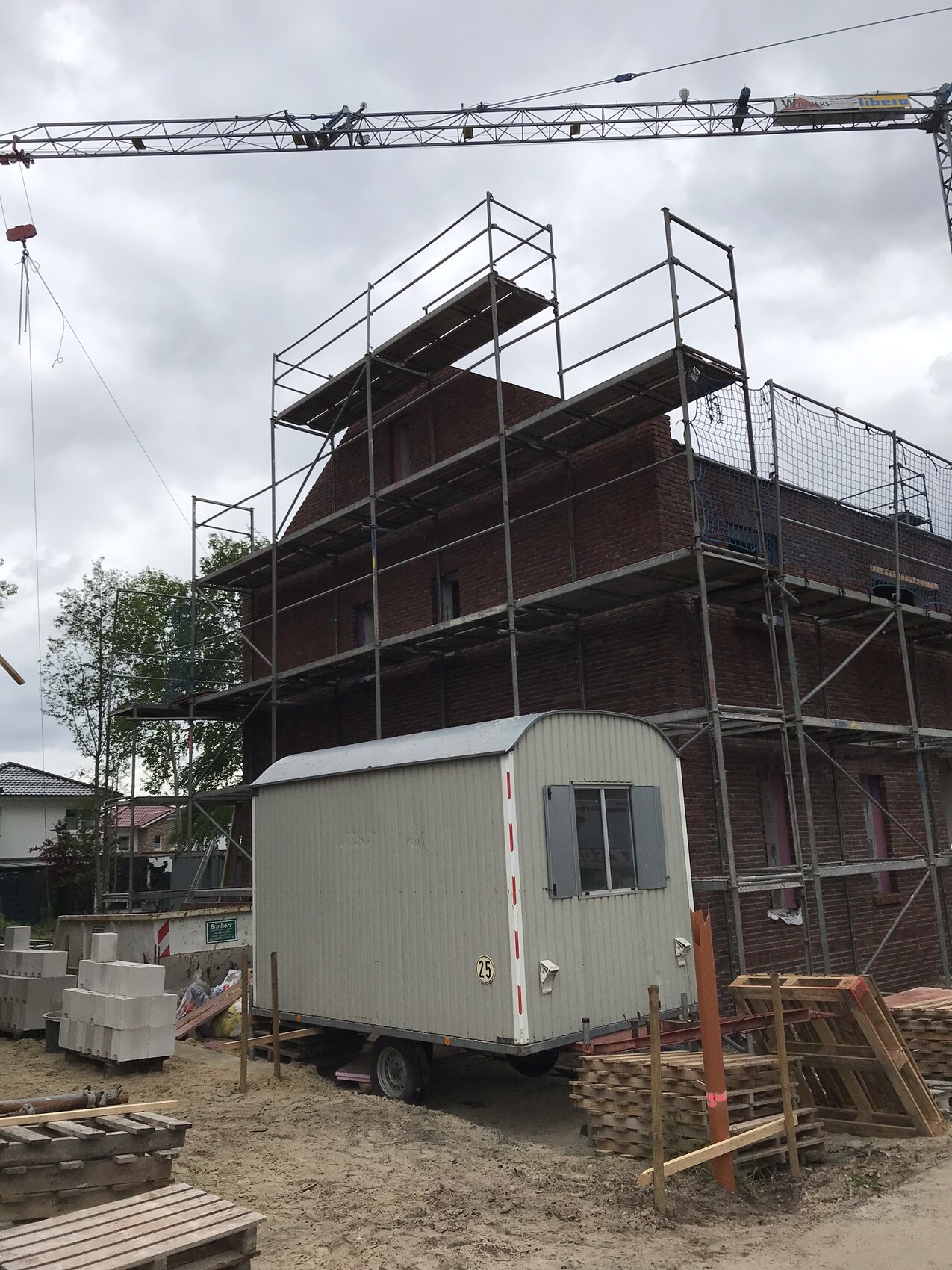 Mehrstöckiger Rohbau mit Gerüst und Baukran auf Baustelle, Container im Vordergrund.