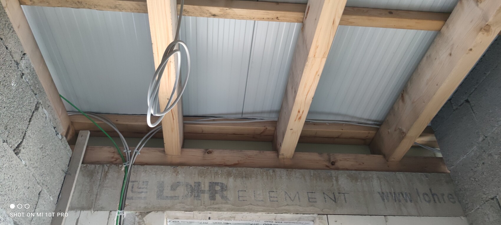Offener Dachstuhl mit Holzbalken, grauen Metall-Dachplatten und lose Kabelschlaufen.