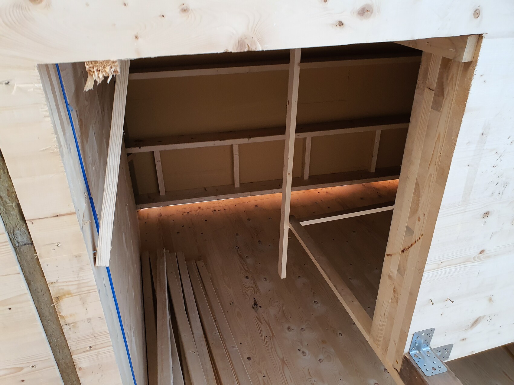 Rohbau: geöffnete Holzwand mit Rahmen, Bodenbretter und Bauholz, hell beleuchtet.