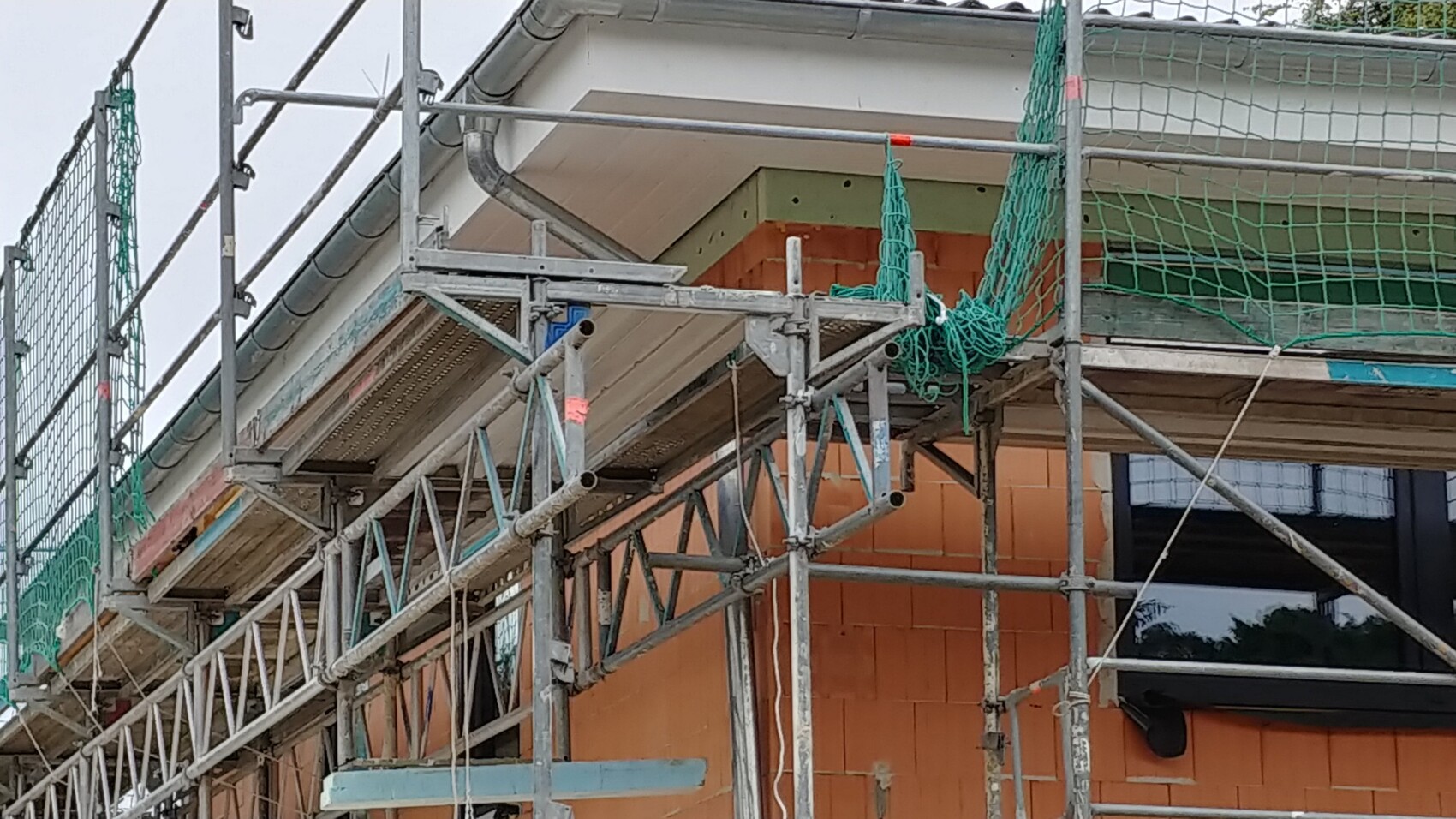 Baustelle mit Baugerüst, grünen Netzen und oranger Ziegelwand