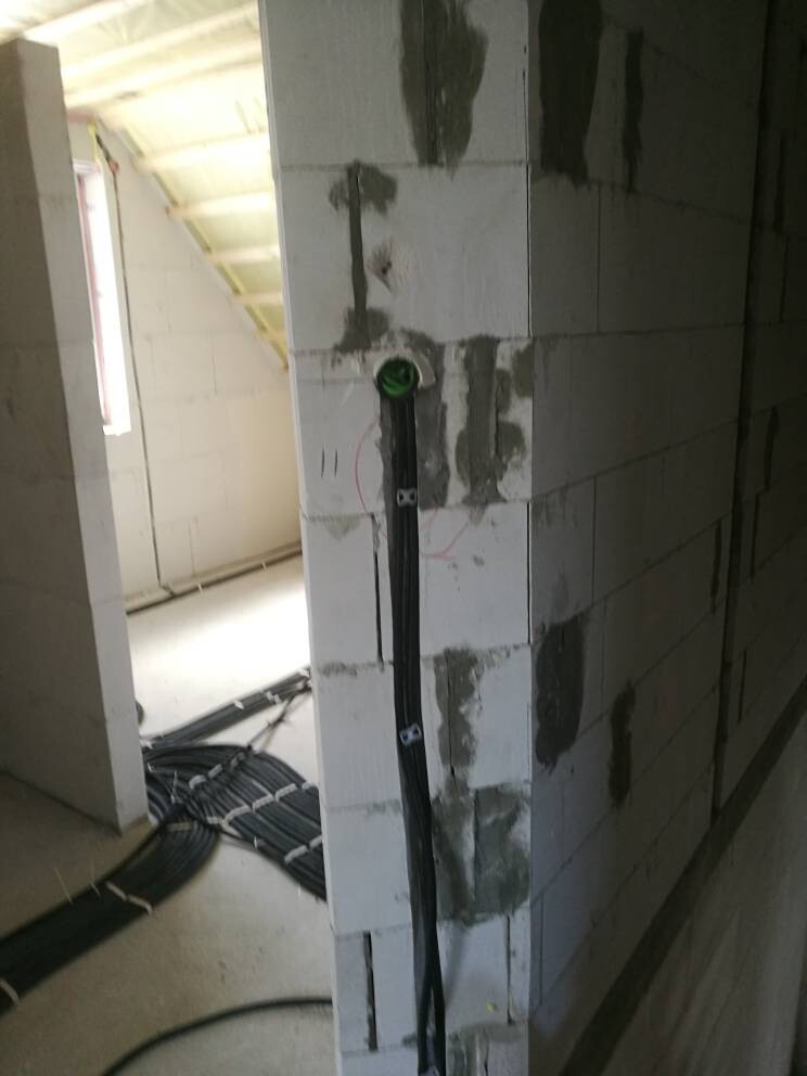 Kabelinstallation in Bauphase: Schwarze Kabelbündel verlaufen senkrecht an einer Wand aus Blöcken.