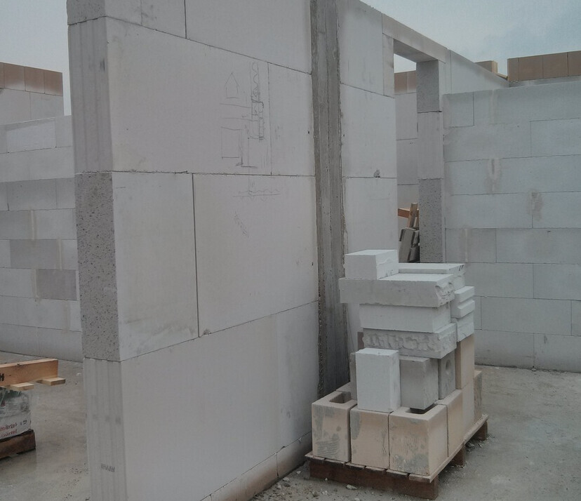 Baustelle mit hellgrauen Betonblöcken; teilweise erbaute Wand, gestapelte Blöcke auf einer Palette