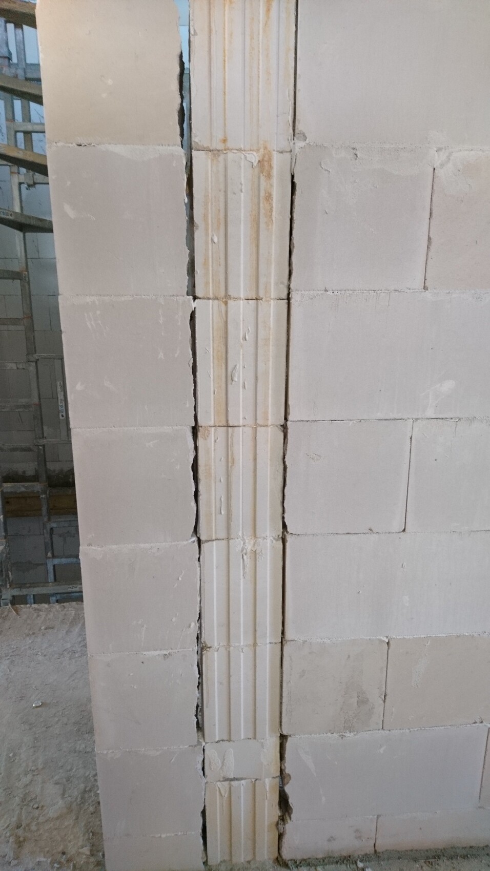 Weiße Betonblockwand mit zentraler vertikaler Profilnut und Rissen