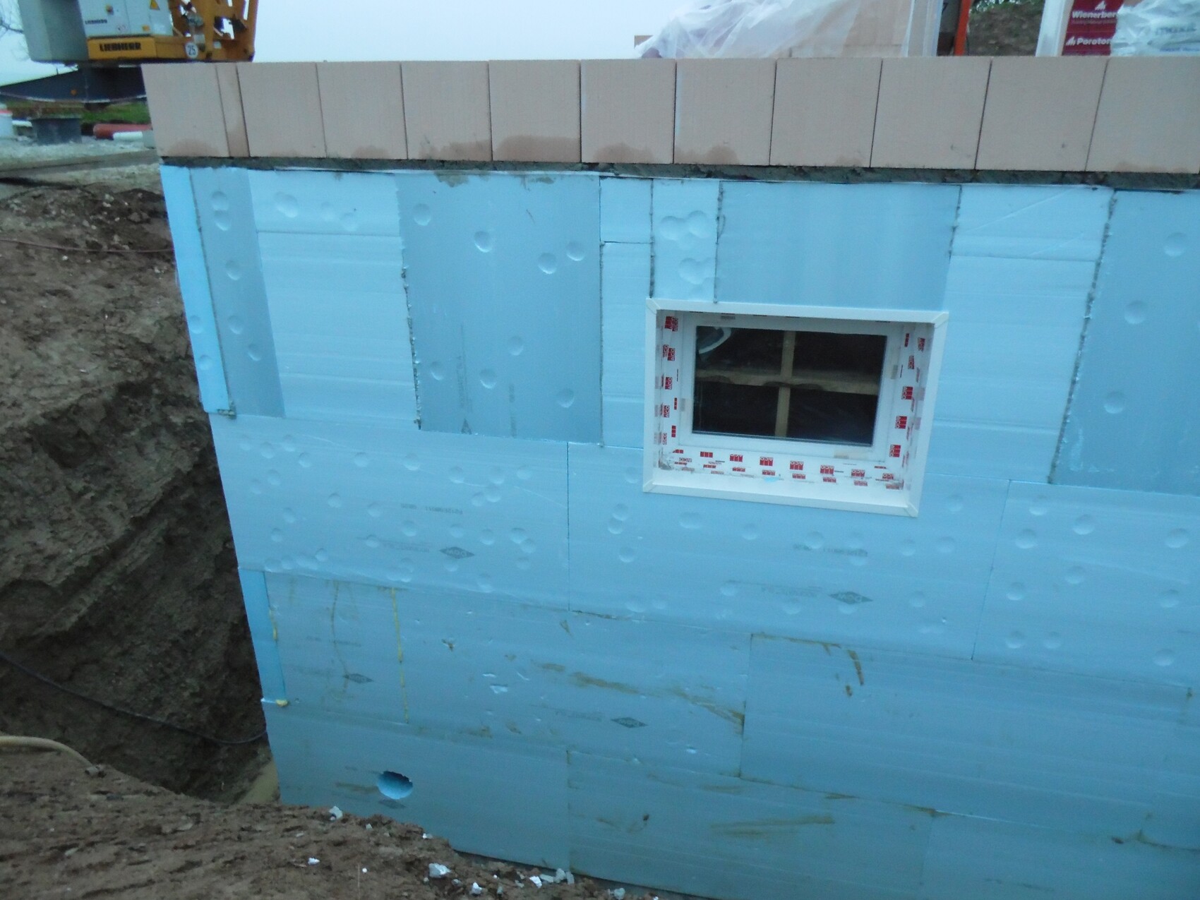 Außenwand im Rohbau mit blauen Dämmplatten und kleinem Fenster.
