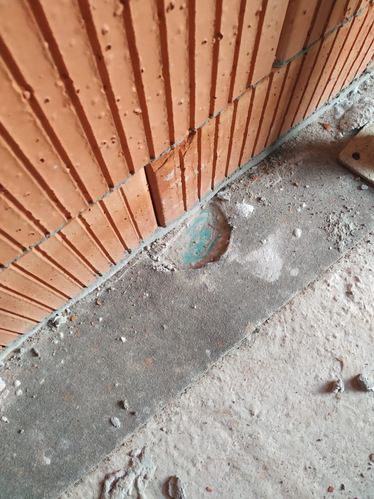Baustellenecke mit roter Ziegelwand, Betonboden und grünem runden Abflussdeckel.