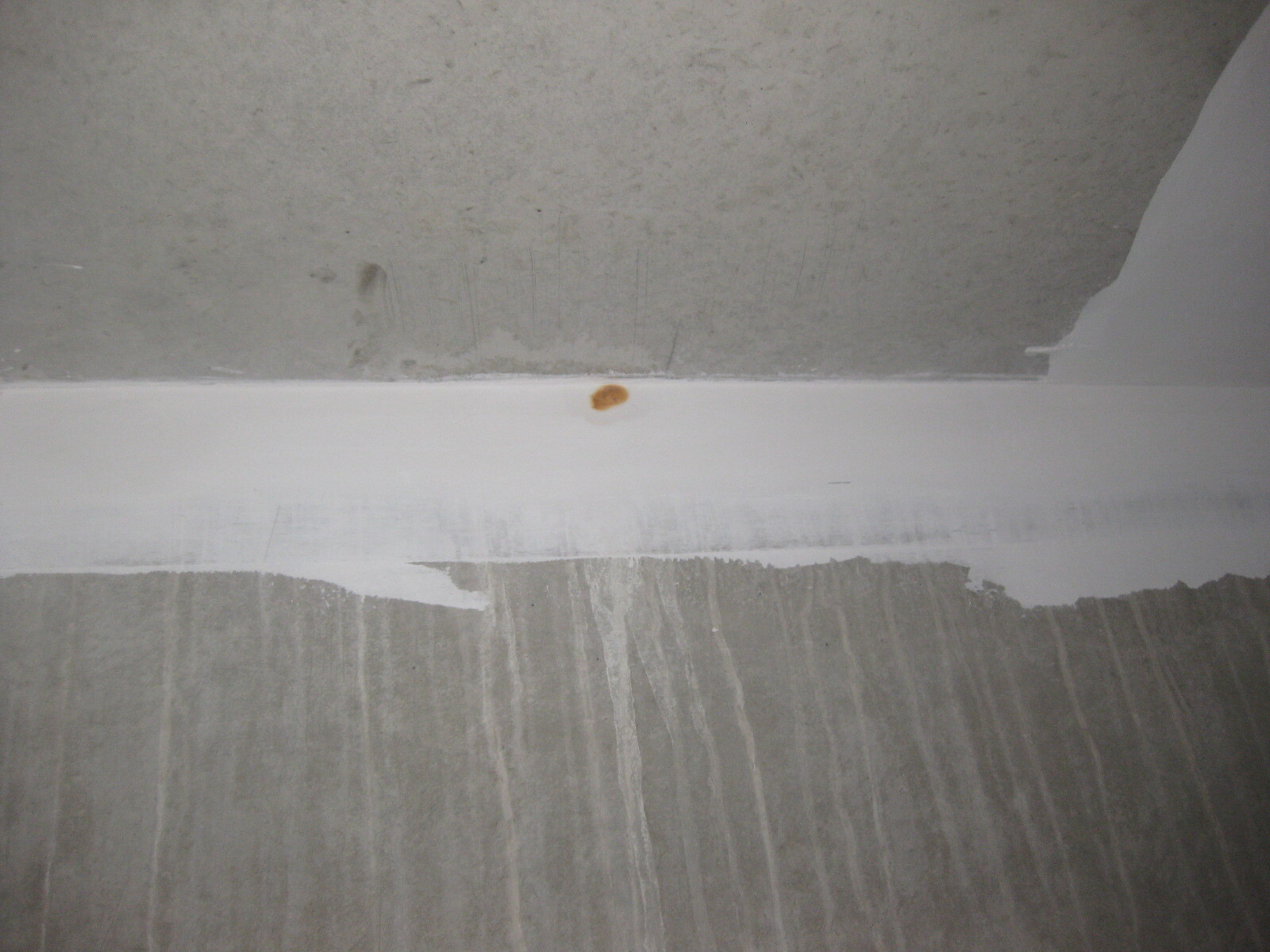 Rohbauwand aus Beton mit weißer Kante und kleinem orangen Fleck