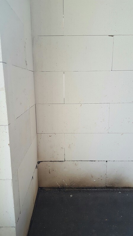 Rohbauwand aus weißen Betonblöcken in einer Ecke eines unfertigen Raums mit dunklem Boden
