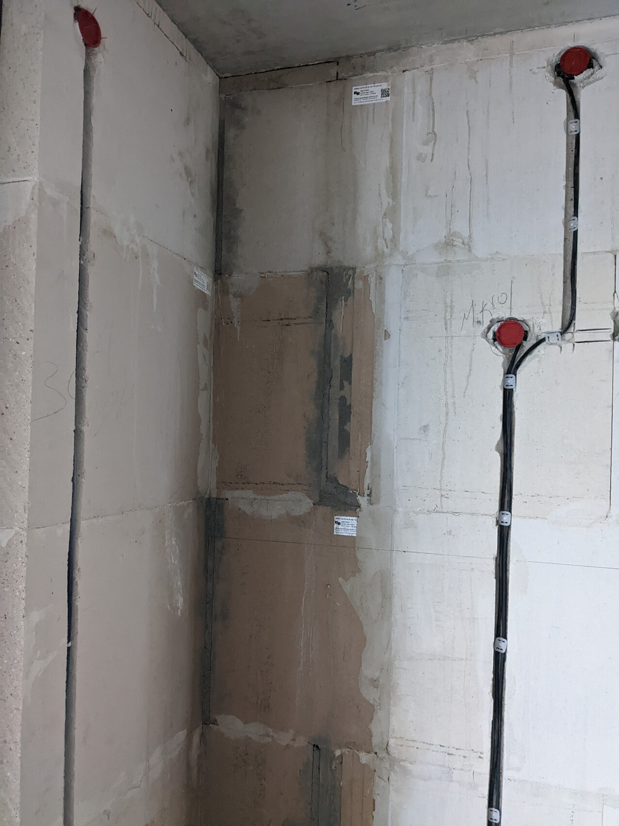 Unfertige Betonwand-Ecke mit Kabelkanälen, roten Abdeckkappen und Putzflächen.