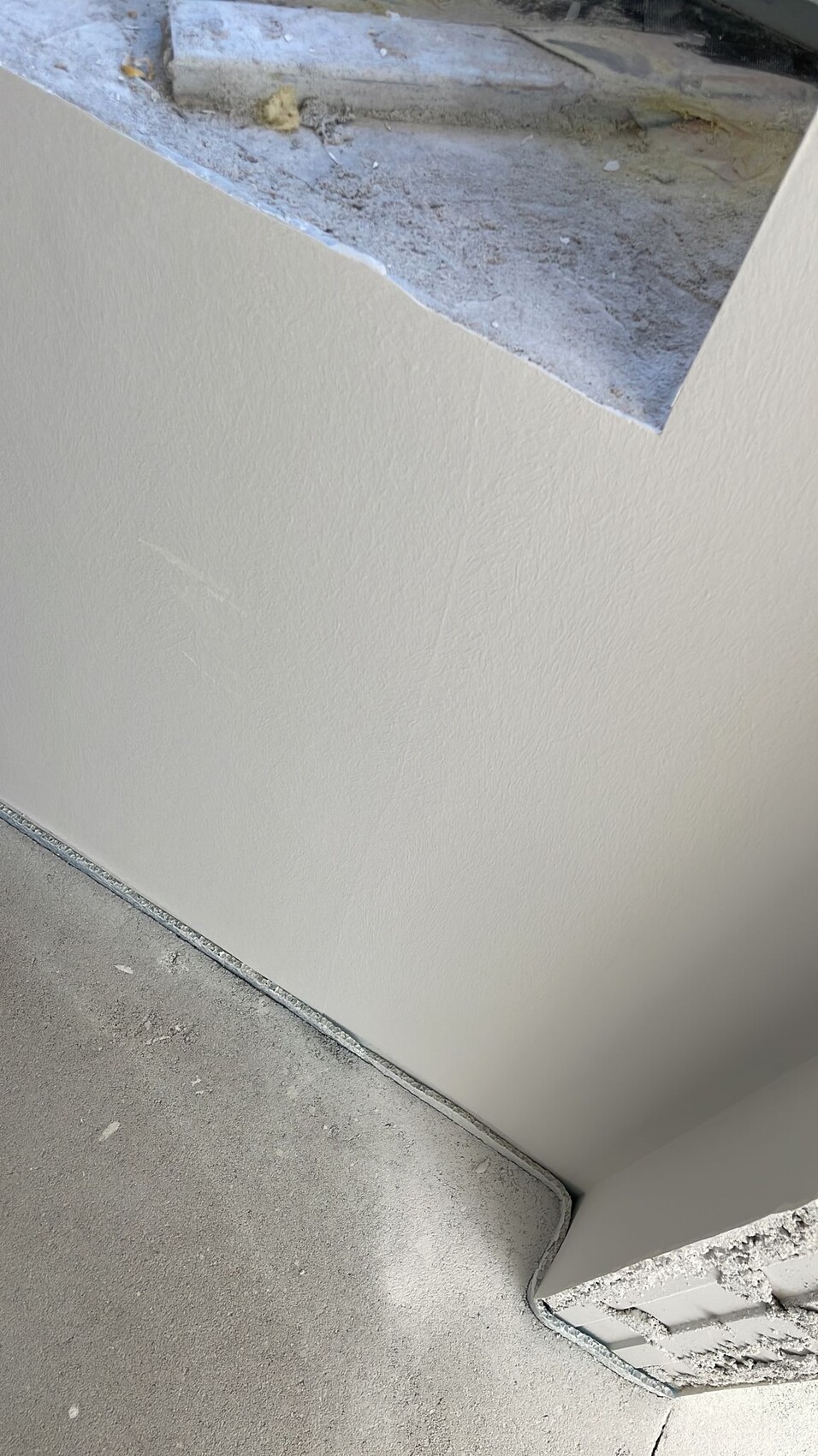 Beige verputzte Innenwand mit rauer Bauöffnung oben und staubigem Boden darunter.