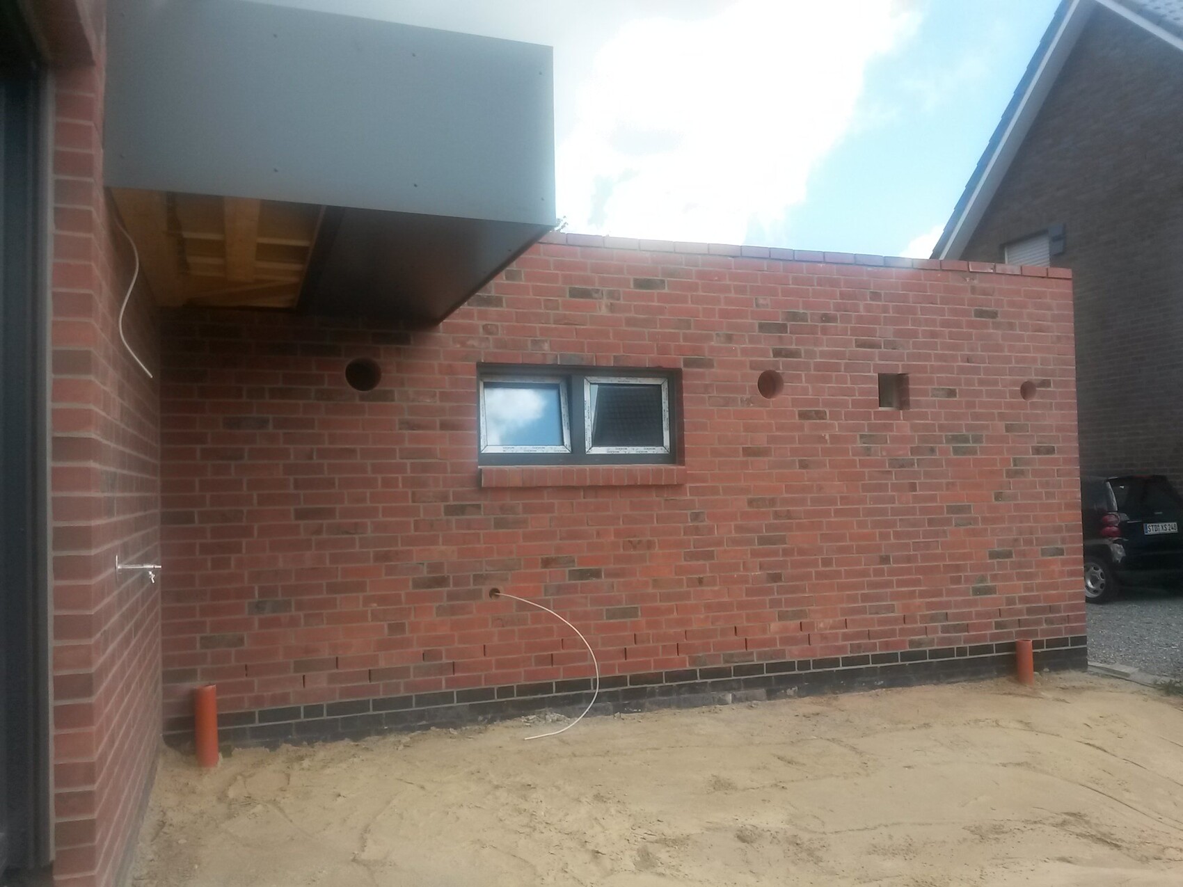 Außenwand aus roten Ziegeln mit kleinem Fenster, Bauarbeiten sichtbar.