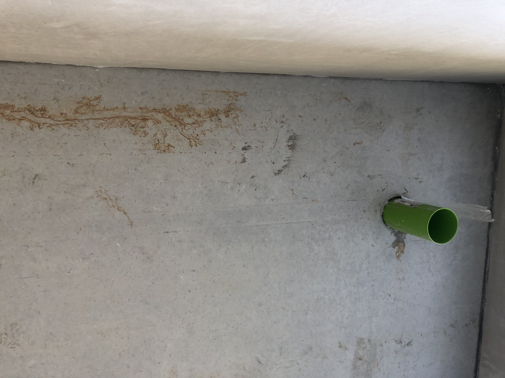 Grüne Rohrleitung ragt aus grauer Betonwand; Rostflecken am Mauerwerk.