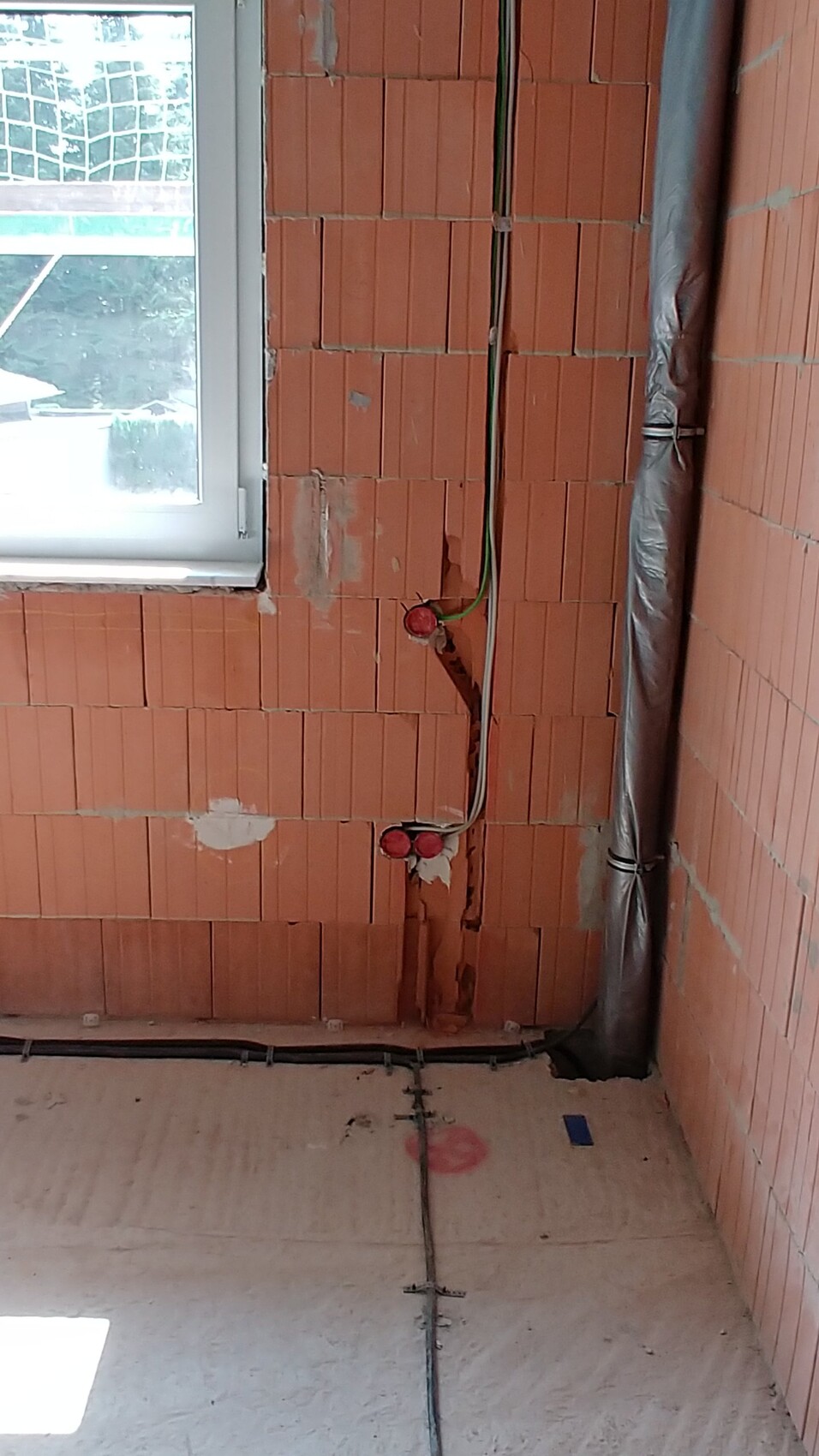 Rohbau Innenraum mit roten Ziegelwänden, sichtbaren Rohren und Fenster