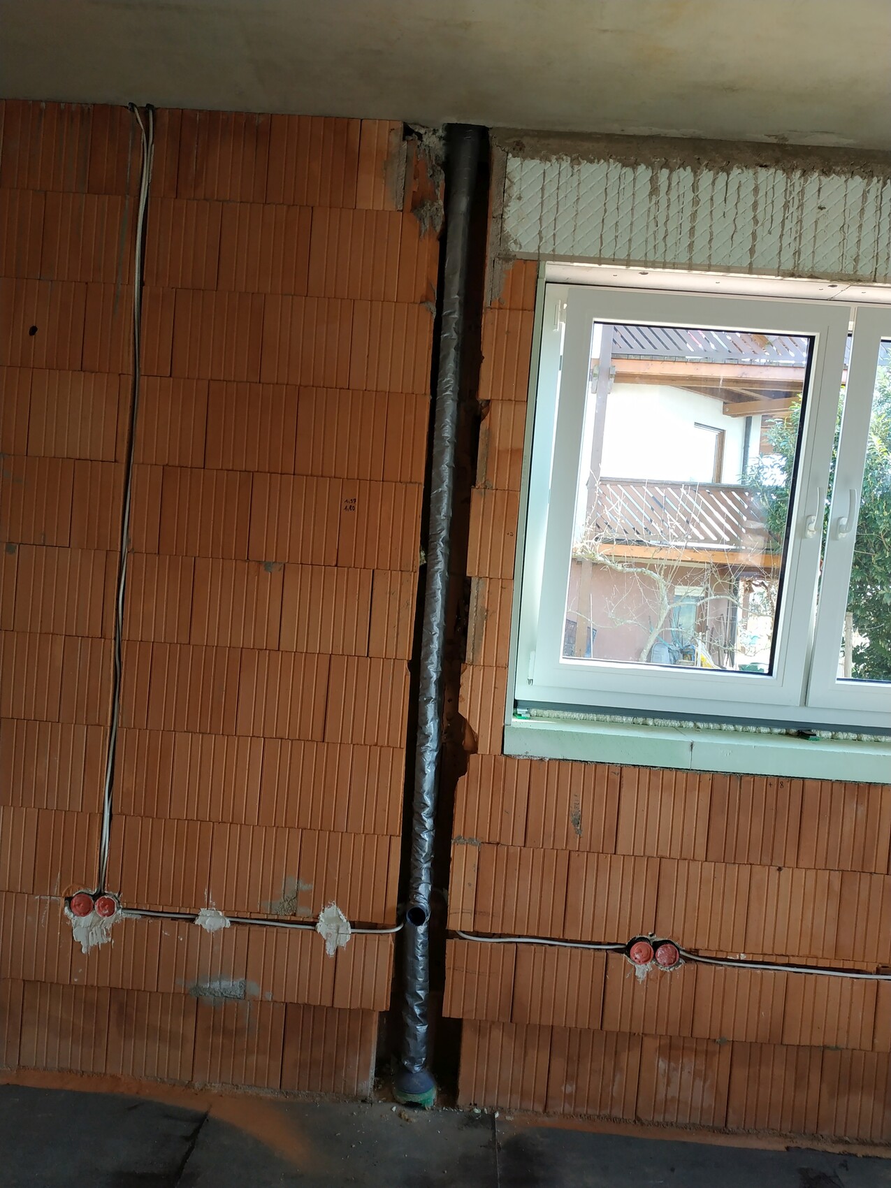 Rohbau-Innenansicht: Ziegelwand, sichtbare Kabel, isoliertes Rohr, Fensterfront