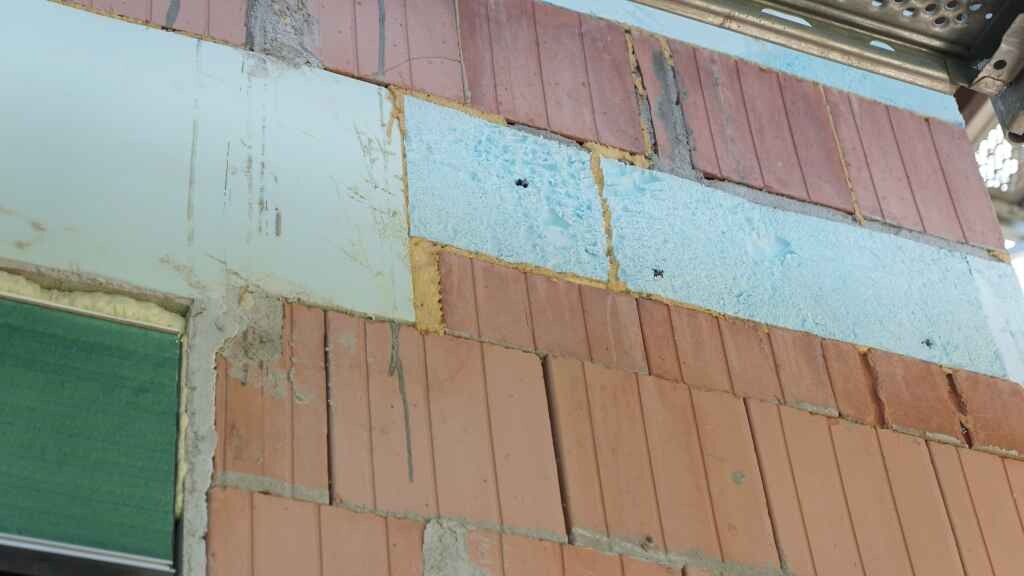 Außenwand aus roten Ziegelsteinen im Rohbau mit heller blauer Dämmplatte