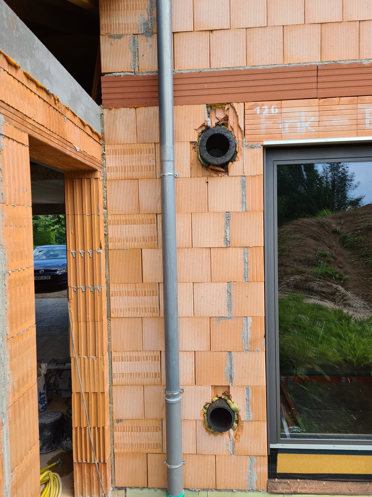 Außenwand aus Ziegelsteinen mit Rohrleitung und runder Öffnung auf Baustelle